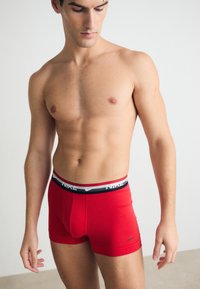 Rote Nike-Badehosen mit einem kontrastierenden schwarzen und grauen Bund. Der Stoff erscheint glatt und elastisch und bietet ein enges Design.