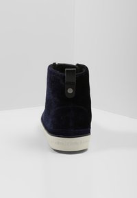 Navy sininen vaskilira-lesti nilkkakenkä valkoisella pohjalla, musta vetonauha nappilla ja "Calvin Klein Jeans" -logo painettuna kantapäässä.