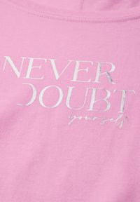 Pink sweatshirt with textured fabric. Features silver foil text stating "NEVER DOUBT yourself" in a mix of bold and cursive styles.