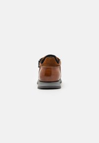 Scarpa in pelle marrone con dettagli in suede, presenta una forma arrotondata, profilo basso e una suola in gomma grigia. La vista posteriore mostra la chiusura con cerniera.