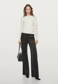 Cream long-sleeve top paired with dark corduroy wide-leg pants. Model holds a black handbag. Smooth and textured fabrics; minimalistic design.