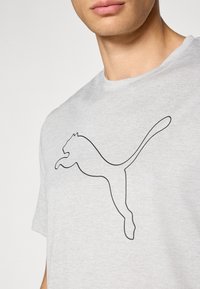 Grå bomulds t-shirt med rund hals, der har en sort kontur af et springende katte logo på forsiden. Korte ærmer, blød tekstur.