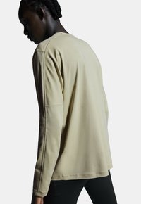 Beige sweatshirt met lange mouwen en een ontspannen pasvorm, ronde halslijn en geborduurde accenten op de mouwen, gedragen over zwarte leggings.