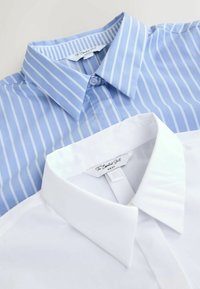 Two collared shirts, one light blue with white stripes and one solid white, displayed with collars overlapping, showcasing smooth fabric textures.