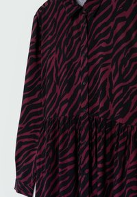 Schwarzes und bordeauxrotes Hemdkleid mit Zebra-Muster. Verfügt über einen Kragen, lange Ärmel und einen gerafften Rock.