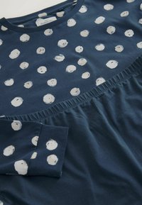 Navy blue maternity top with white polka dot pattern, round neckline, gathered waistline, and soft cotton material. Features long sleeves.