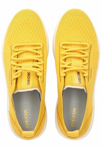 Gelbe Sportschuhe mit einem(mesh) Obermaterial und synthetischen Akzenten. Sie verfügen über flache Schnürsenkel, eine gepolsterte Innensohle und eine weiße Gummisohle.