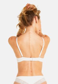 Soutien-gorge blanc avec bretelles réglables, texture de tissu douce, fermeture crochets-oeil à l'arrière, et design minimaliste.