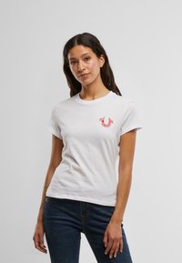 Witte katoenen t-shirt met een ronde halslijn en korte mouwen. Bevat een klein rood logo op de linkerborst. Klassieke pasvorm met een gladde textuur.