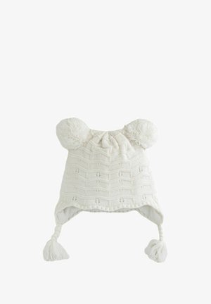 Hvid strikket hat med pom-pomer, struktureret mønster, øreklapper og flettræk med kvaster. Blødt, hyggeligt stof til varme.