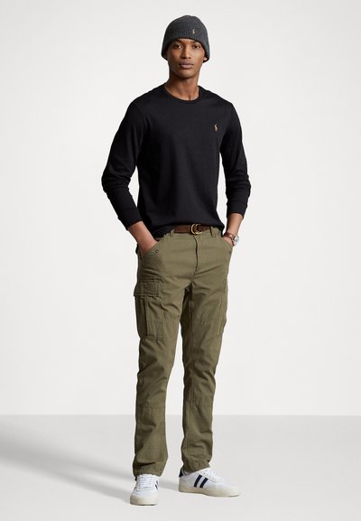 Melnas garajām piedurknēm krekls, olīvzaļi kravas bikses, pelēks adīts beanie un baltas kedas ar jūras zilām svītrām. Slim fit ar kabatām biksēm.