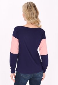 Tengerészkék hosszú ujjú póló rózsaszín színblokkolt ujjakkal és gombos részletekkel. Puha anyag, kerek nyak, és lazább fazon.