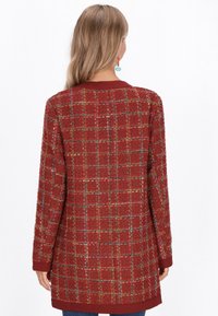 Giacca rossa con texture e motivo a scacchi, maniche lunghe e colletto borgogna. Il tessuto presenta fili multicolori intrecciati nel design.