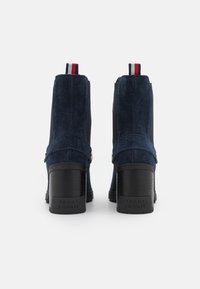 Botines de ante en color marino con tacón cuadrado negro, paneles laterales elásticos y una lengüeta de tirón a rayas en rojo, blanco y azul. Marca en el tacón.