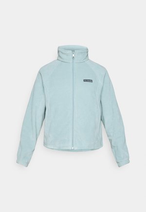 Jachetă fleece de culoare albastru deschis, cu guler înalt, fermoar central și design cu panouri laterale. Include o etichetă cu logo negru pe partea stângă a pieptului.