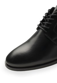 Chaussure habillée en cuir noir avec une finition brillante, bout rond et fermeture à lacets. Présente des coutures discrètes et une semelle texturée.