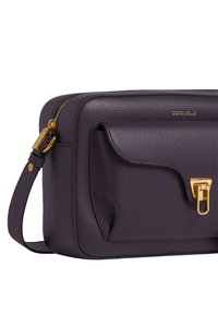 Borsa a tracolla in pelle viola con chiusura dorata, zip in alto e tasca frontale. Superficie testurizzata e tracolla regolabile.