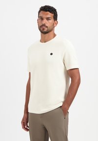 Korte mouwen crèmekleurig textiel shirt met een ronde hals, met een klein zwart hexagonaal logo op de borst. Gekocht met beige broek.