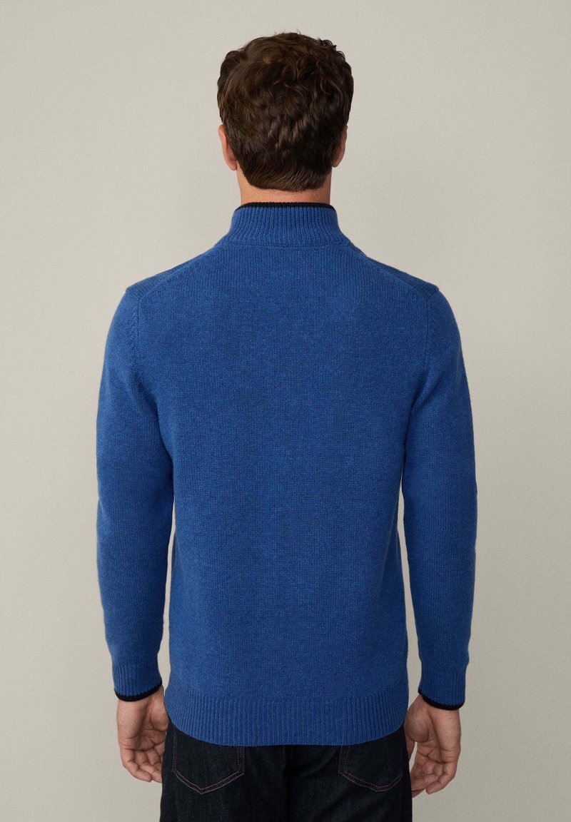 Pull en tricot bleu avec un col montant, des poignets et un ourlet côtelés. Texture douce avec un motif uni, design ajusté.