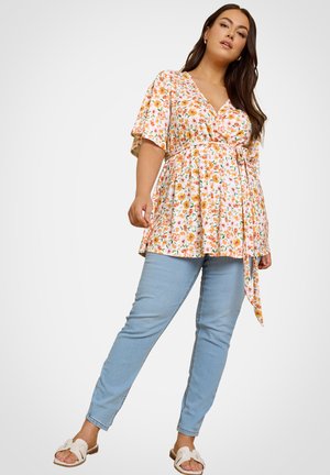 White floral top with orange and green patterns, v-neck, short sleeves, cinched waist, and tie detail; paired with light blue jeans and sandals.