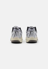 Pár šedých a černých tenisek Nike Air Pegasus z pohledu zezadu na bílém pozadí.