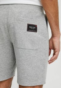 Grå bomulds shorts med en baglomme, der har en sort og rød mærketiket. Stofmet har et blødt, struktureret udseende.