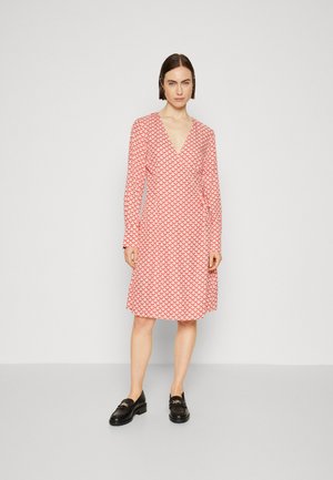 Red patterned dress with a V-neck and long sleeves; fabric features a wavy scale design; model paired with black loafers.