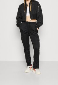 Svart kort bomberjacka med dragkedja, åtsittande svarta cargo-byxor med sidfickor, bärs med vita sneakers och röda accenter.