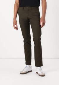 Mørkegrønne chinos med slim fit, der har frontlommer, knaplukning og er parret med hvide sneakers. Glat bomuldsstof.