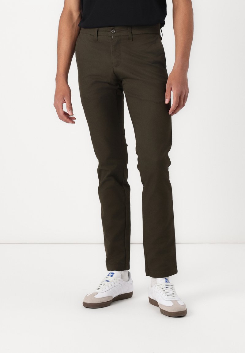 Mørkegrønne chinos med slim fit, der har frontlommer, knaplukning og er parret med hvide sneakers. Glat bomuldsstof.