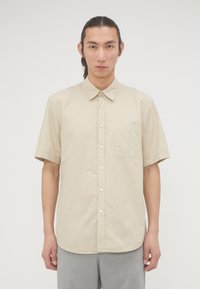 Beige overhemd met korte mouwen, gemaakt van een gladde stof, met een knoopsluiting aan de voorkant, een kraag en een borstzak. Eenvoudig ontwerp, zonder patronen.