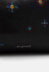 Czarny skórzany portfel z kolorowymi haftowanymi wzorami roślinnymi w kolorach niebieskim, turkusowym, żółtym, czerwonym oraz srebrnym wytłoczonym logo.