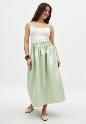 Groene satijnen maxirok met gegomde taille, gladde textuur, uitlopende vorm en enkellengte. Gemaakt met een wit tanktop en platte schoenen.
