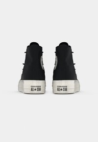 Schwarze High-Top-Sneaker mit einem glatten Obermaterial aus Stoff, weißer Gummisohle, auffälligem Logo-Patch und Ösen-Schnürdetail auf der Rückseite.