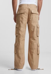 Khaki cargo pants with multiple side pockets, a loose fit, and drawstring cuffs. Made from breathable fabric with a smooth texture.