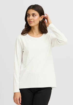 Vit långärmad t-shirt i mjukt, slätt tyg med rund halsringning och avslappnad passform, kombinerad med svarta byxor. Inga framträdande mönster eller detaljer.