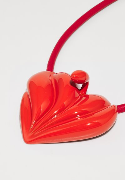 Colgante rojo en forma de corazón con un acabado brillante, que presenta un diseño curvado y acanalado. Suspendido en un cordón rojo liso.