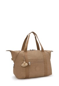 Tan canvas duffel bag with dual handles, zip closure, front pocket, round logo patch, and a furry charm attached. Smooth texture with structured shape.