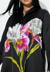 Sort satinbluse med farverigt blomsterprint i pink, hvid og grøn, med knaplukning og glat tekstur.