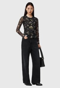 Μαύρο διαφανές τοπ με λουλουδάτο μοτίβο και μακριά μανίκια, συνδυασμένο με μαύρο τζιν παντελόνι φαρδιάς γραμμής και ψηλόμεσο. Διακοσμημένο με ζώνη με αγκράφα και μαύρη τσάντα.