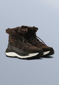 Ghete de drumeție maro cu partea superioară texturată, guler strâns și șireturi negre. Talpă groasă albă și neagră, cu un design robust al profilului.