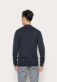 Maglione a maniche lunghe blu navy, collo tondo, polsini e orlo a coste, tessuto liscio, design aderente, visto da dietro.