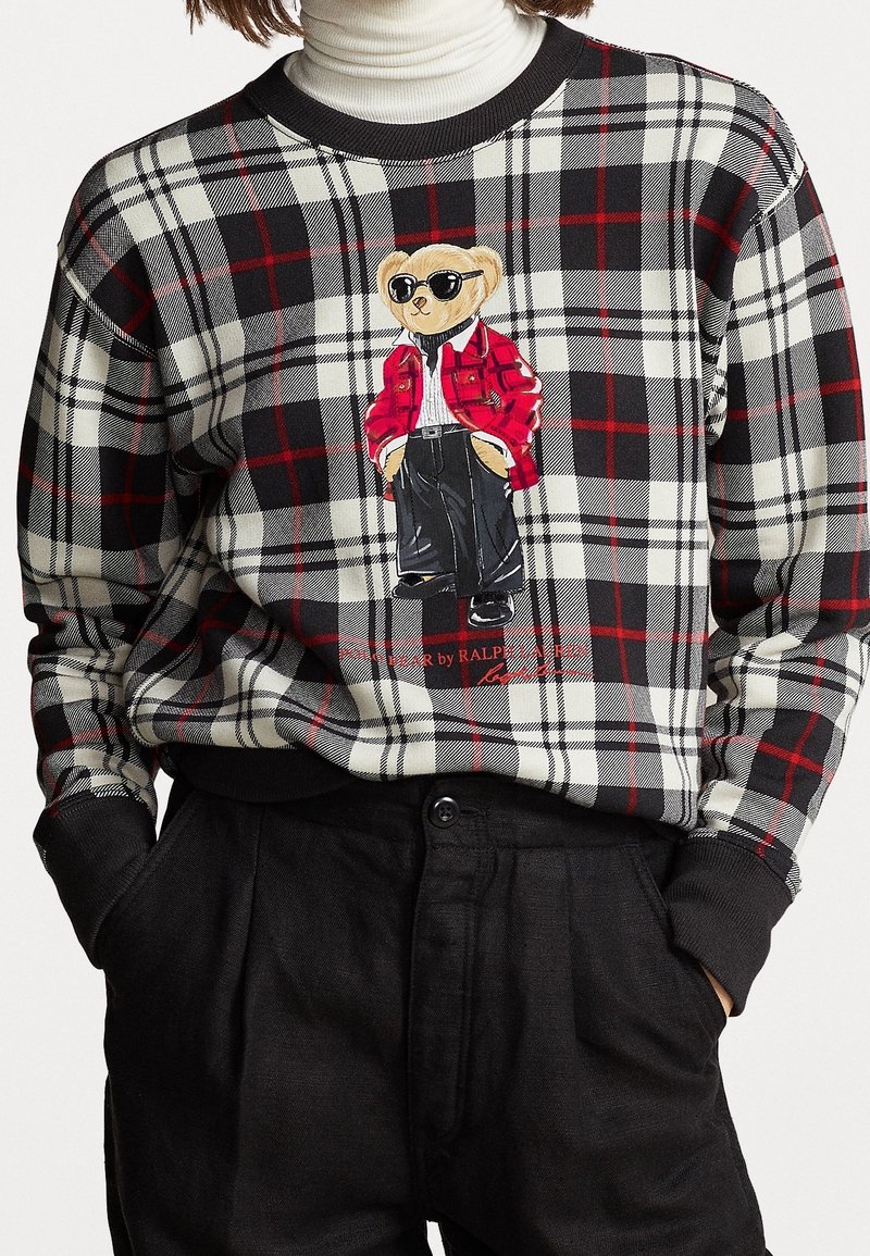 Pull à carreaux noir, blanc et rouge avec un ours en peluche portant des lunettes de soleil, une veste rouge et un pantalon noir imprimés sur le devant.