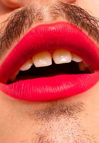 Jasnoczerwone usta z matowym wykończeniem, ukazujące proste białe zęby i lekko otwarte usta. Dark zarost jest widoczny nad ustami.