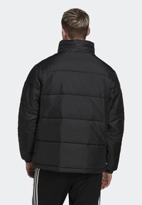 Czarna kurtka puchowa z pikowanym wzorem, wysokim kołnierzem i przednim suwakiem. Materiał o fakturze i elastyczne mankiety, w zestawieniu z czarnymi spodniami sportowymi.