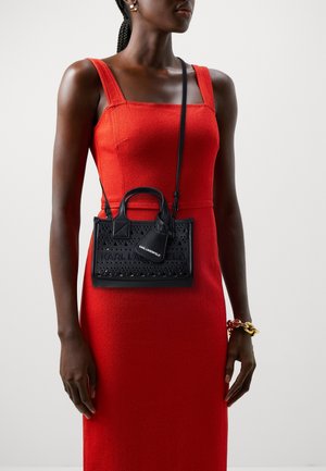 Mujer con un vestido rojo sin mangas, complementado con pendientes de aro dorados, una pulsera gruesa de oro y un bolso bandolera negro de Karl Lagerfeld.