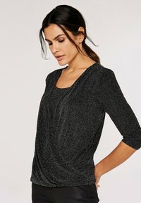 Sort, struktureret top med rund halsudskæring og trekvartærmer. Stoffet har en subtil glans, der tilføjer visuel interesse til designet.