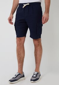 Shorts cargo bleu marine avec une taille à cordon, dotés de deux poches latérales et d'un tissu doux et texturé. Portés avec des baskets grises et bleu marine.