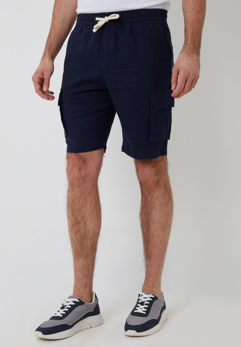 Shorts cargo bleu marine avec une taille à cordon, dotés de deux poches latérales et d'un tissu doux et texturé. Portés avec des baskets grises et bleu marine.