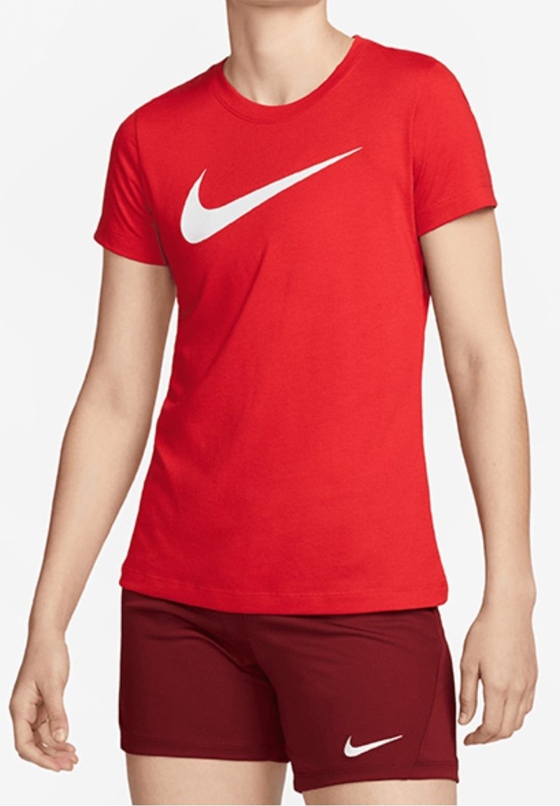 Henkilö, joka on pukeutunut punaiseen Nike-paitaan ja tummanpunaiseen Nike-shortsien, seisoo yksinkertaista valkoista taustaa vasten.